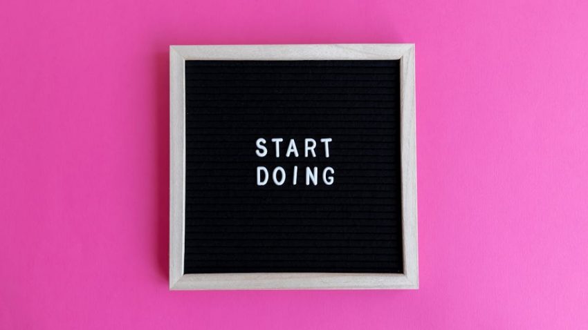 Black letter board with 'Start Doing' motivational text on bright pink background.